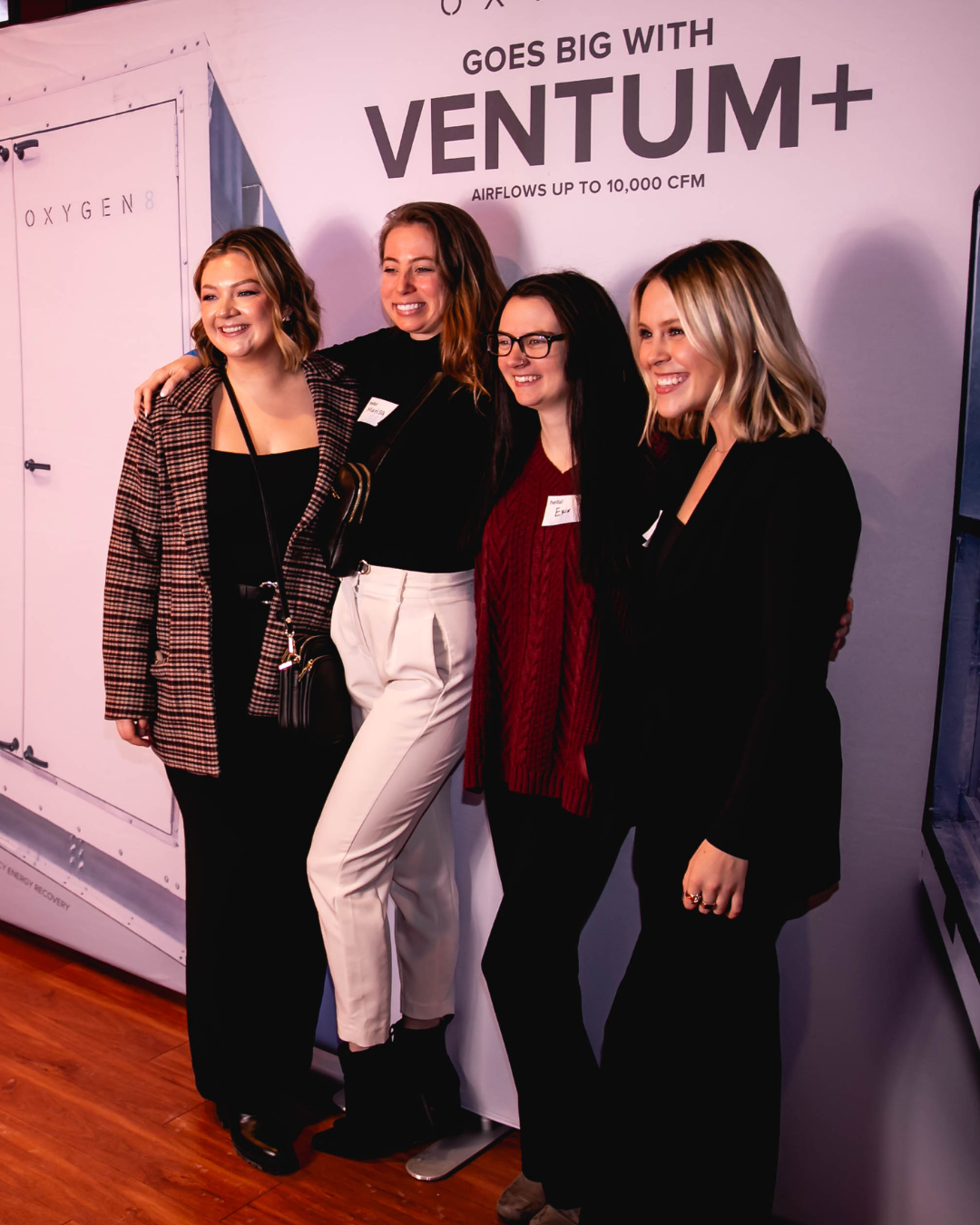 Group of coworkers stand in front of branded step and repeat for a photo