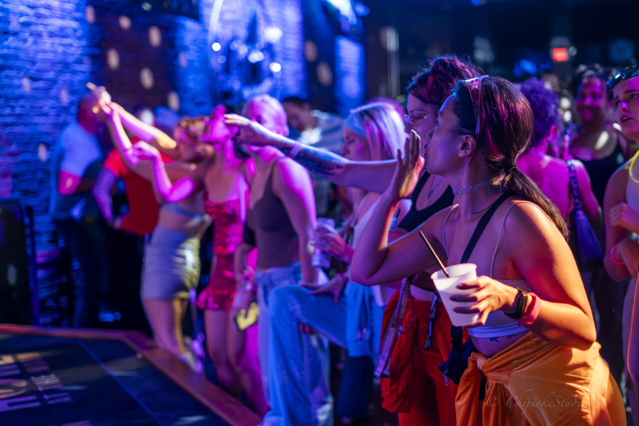 Crowd dancing and singing along with drinks in hand at a 2000’s Throwback Party in a vibrant nightclub.
