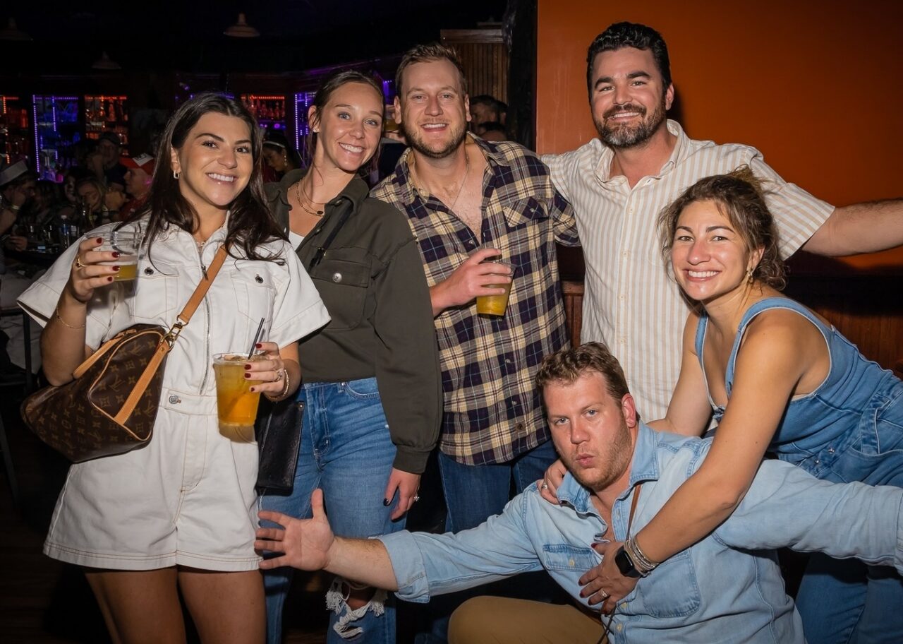 Group of friends posing with drinks at a Dad Rock Music Party with classic rock and divorced dad rock music vibes at a lively bar. Dad Rock Music Party.