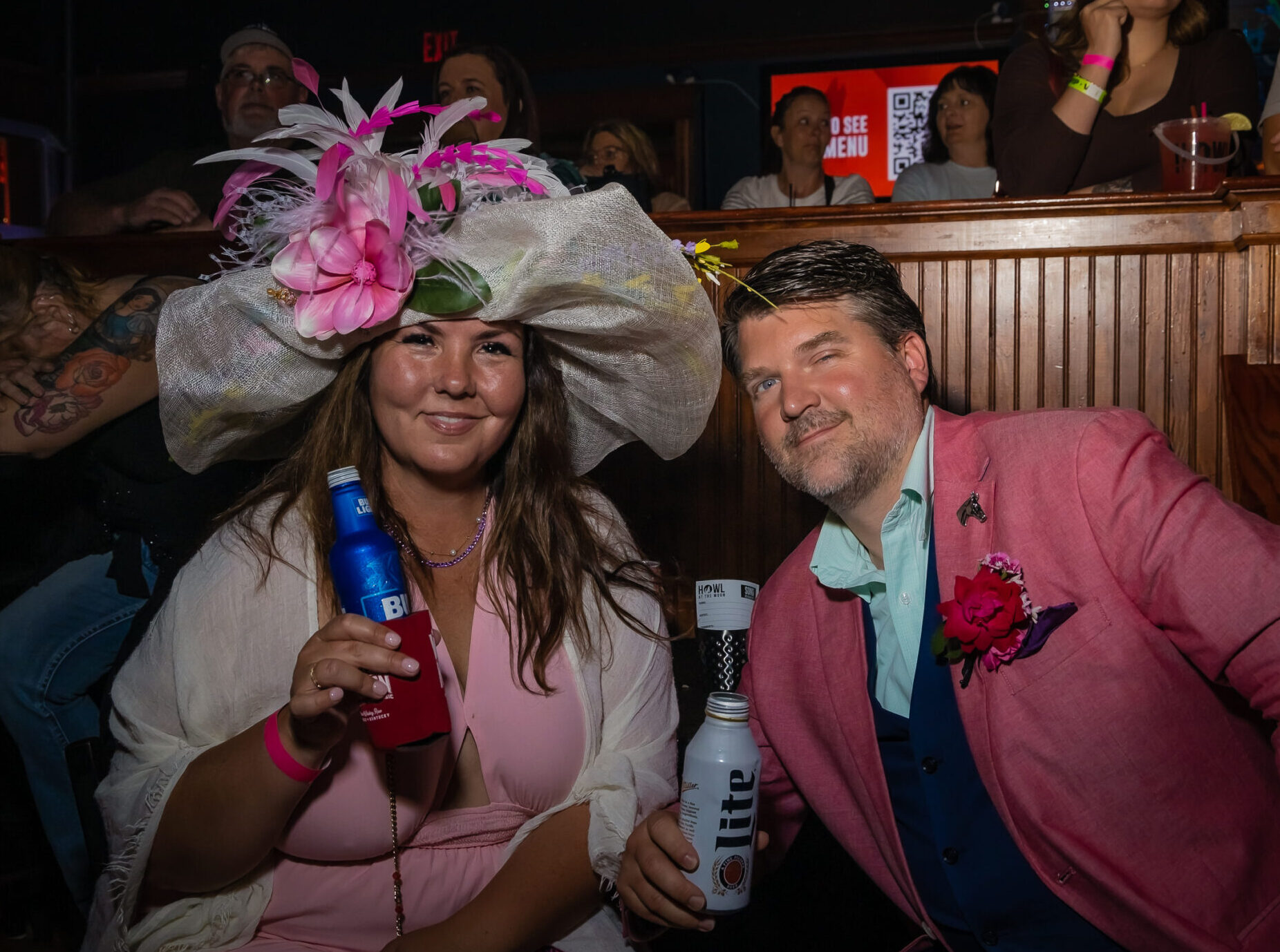 Couple celebrating Kentucky Derby weekend at Howl at the Moon Louisville wearing a Derby hat and pink blazer while enjoying drinks at the Louisville Derby party.