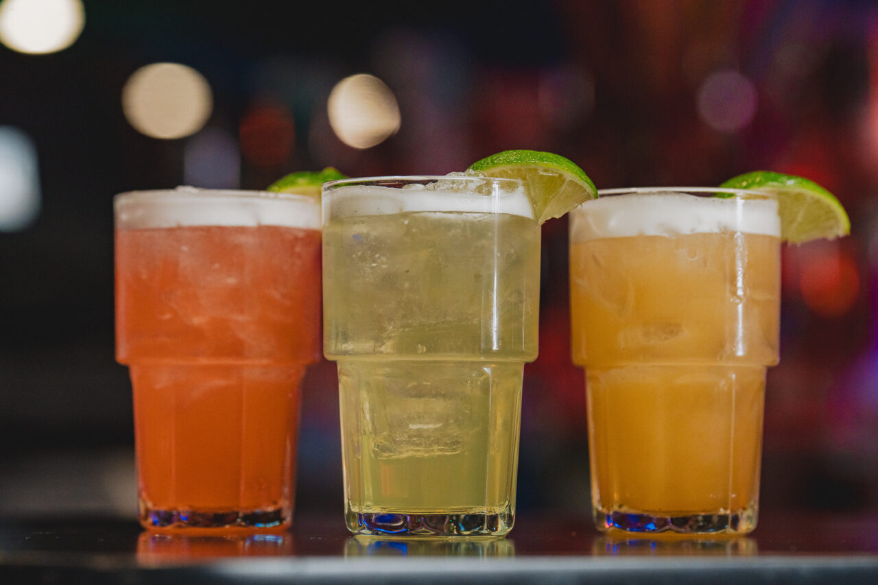 Three margarita cocktails with lime wedges on a bar at Howl at the Moon, featuring colorful drinks for Cinco de Mayo specials