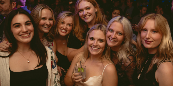 Group of college graduates celebrating together at Howl at the Moon with drinks, smiling and posing during a lively graduation party night out