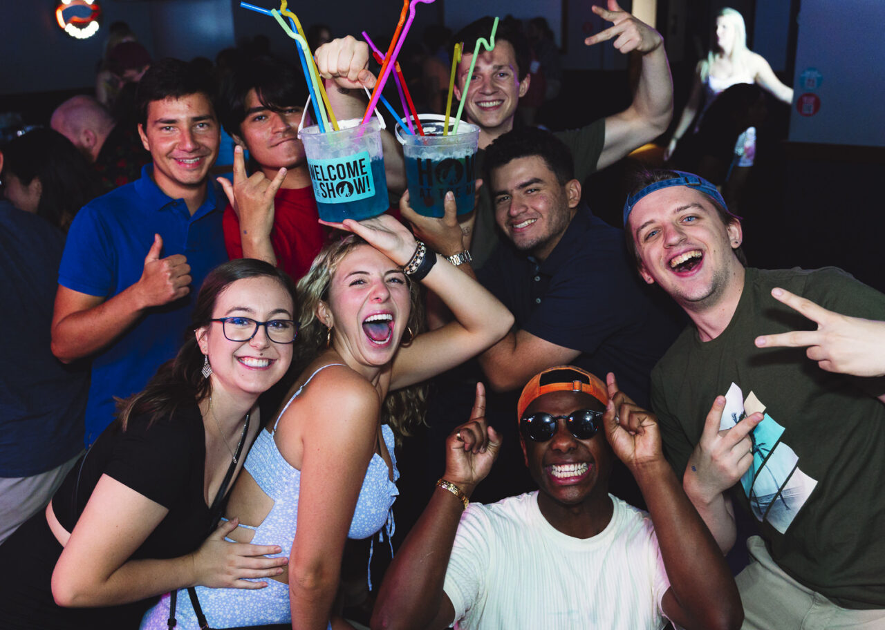 Group of friends posing with oversized bucket drinks during Happy Hour at Howl at the Moon.